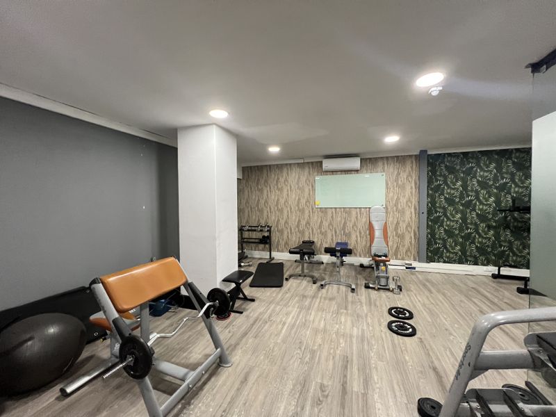 A functional office gym space featuring laminate flooring, recessed lighting, a wall-mounted air conditioning unit, and a whiteboard.