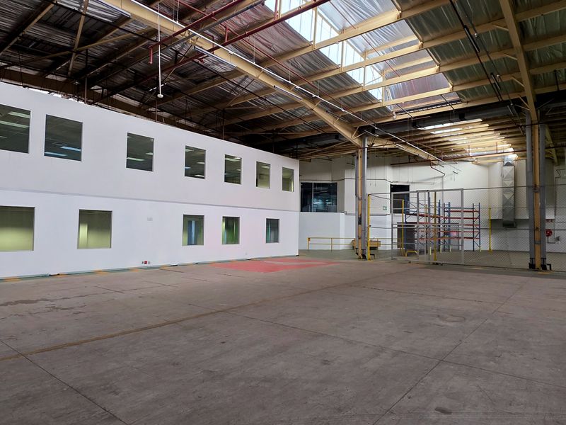 Spacious industrial warehouse featuring high ceilings with skylights, concrete flooring, and an integrated two-story office block with partitioned windows.