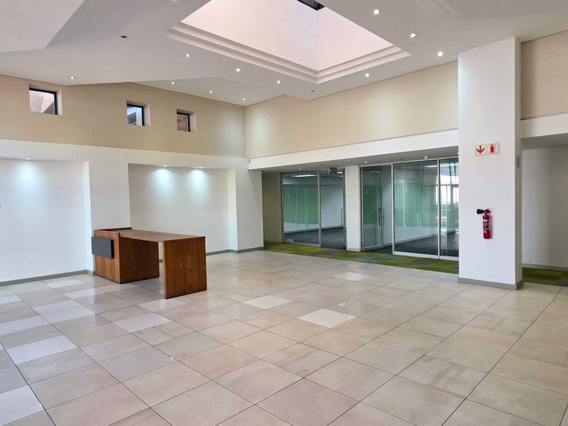Spacious industrial entrance lobby featuring tiled flooring, recessed ceiling lighting, a central skylight, and glass-partitioned office access.