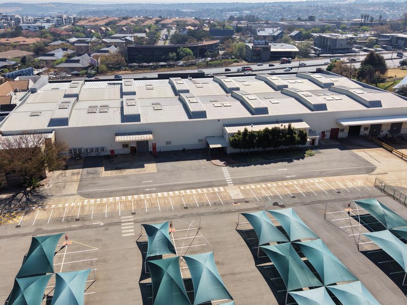 Aerial view of a large industrial warehouse facility featuring extensive parking, shade cloth carports, loading bays, and a well-maintained roof structure.