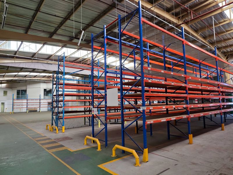 Spacious industrial warehouse featuring high ceilings with skylights, concrete flooring, and extensive built-in steel racking systems for efficient storage.