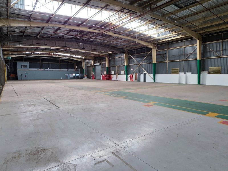 Spacious industrial warehouse featuring high ceilings with integrated skylights, concrete flooring, and robust steel portal frame construction, suitable for storage or manufacturing operations.