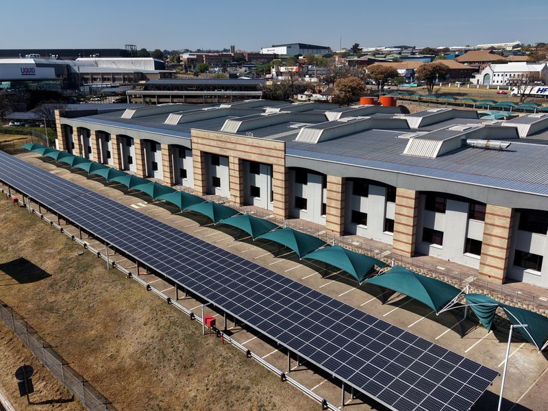 Aerial view of an industrial facility featuring extensive solar panel arrays over parking areas and a well-maintained building structure.