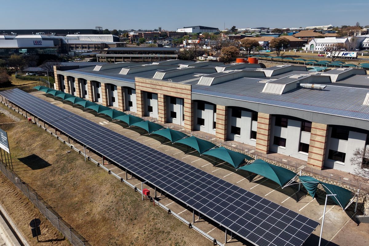 Aerial view of an industrial facility featuring extensive solar panel arrays over parking areas and a well-maintained building structure.