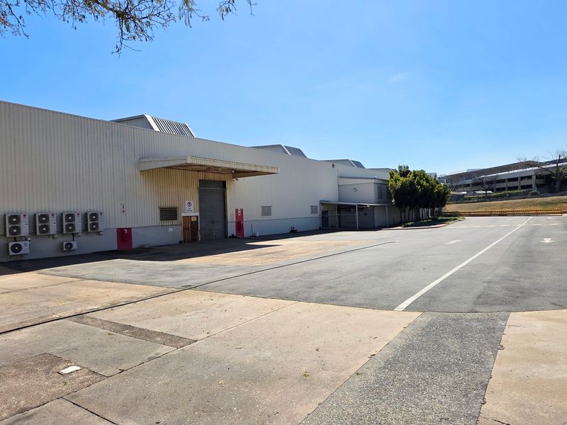 Rear industrial yard featuring a large asphalt loading area, metal-clad building facade, and multiple external air conditioning units.