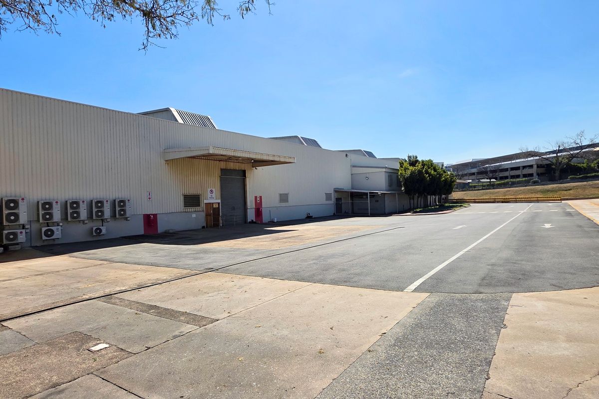 Rear industrial yard featuring a large asphalt loading area, metal-clad building facade, and multiple external air conditioning units.