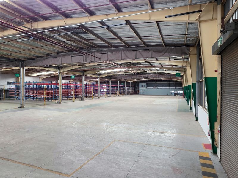 Spacious industrial warehouse featuring a high-clearance steel portal frame, concrete flooring, fire sprinkler system, and a large roller shutter door for easy access.