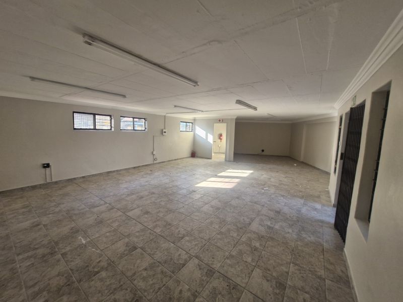 Spacious, open-plan commercial interior featuring durable tiled flooring, fluorescent lighting, and secure access points, suitable for various business or office configurations.