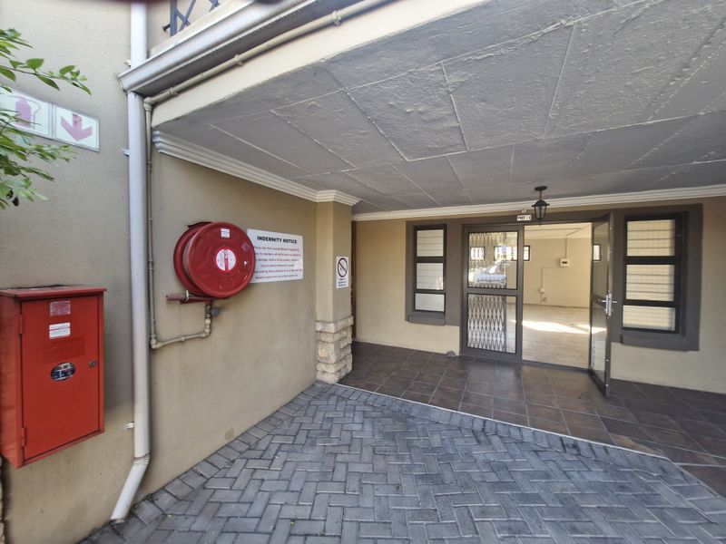 Commercial entrance area featuring a paved driveway, tiled porch, security gate, and essential fire safety equipment including a hose reel and hydrant cabinet.