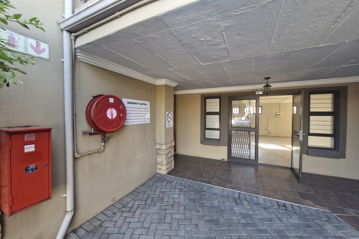 Commercial entrance area featuring a paved driveway, tiled porch, security gate, and essential fire safety equipment including a hose reel and hydrant cabinet.