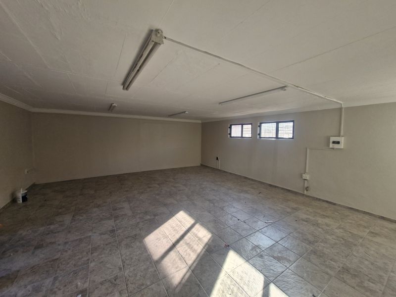 A spacious, empty commercial office area featuring tiled flooring, fluorescent lighting, and secure windows, suitable for various business configurations.