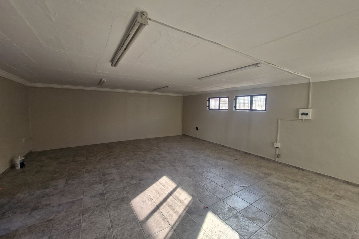 A spacious, empty commercial office area featuring tiled flooring, fluorescent lighting, and secure windows, suitable for various business configurations.