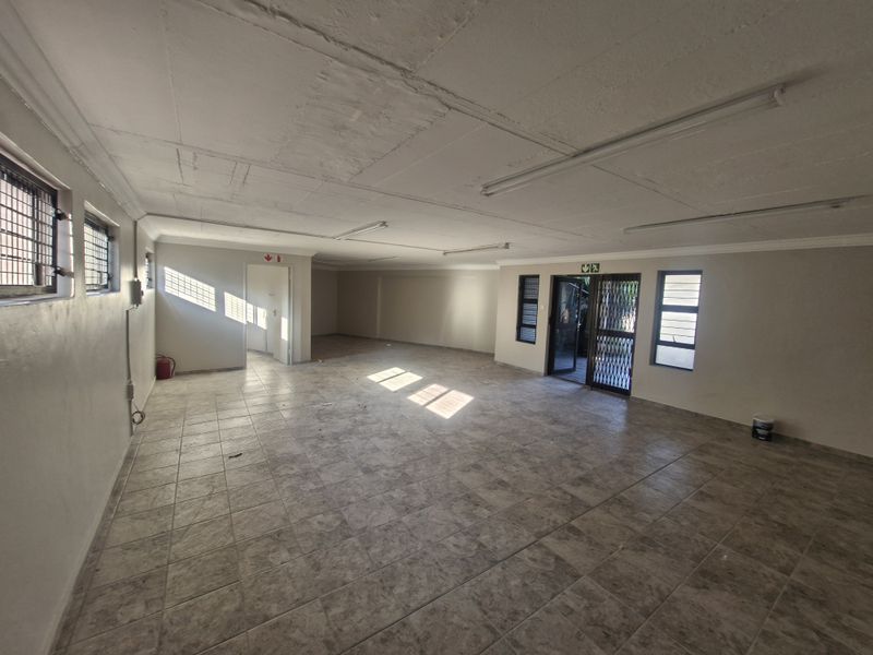 Spacious open-plan commercial area featuring tiled flooring, security gates, and natural light, suitable for office or retail use.