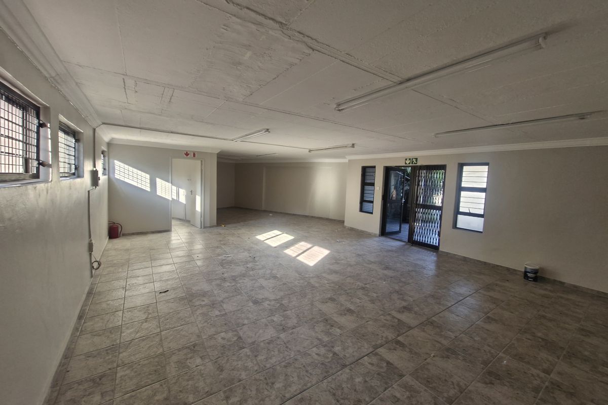 Spacious open-plan commercial area featuring tiled flooring, security gates, and natural light, suitable for office or retail use.