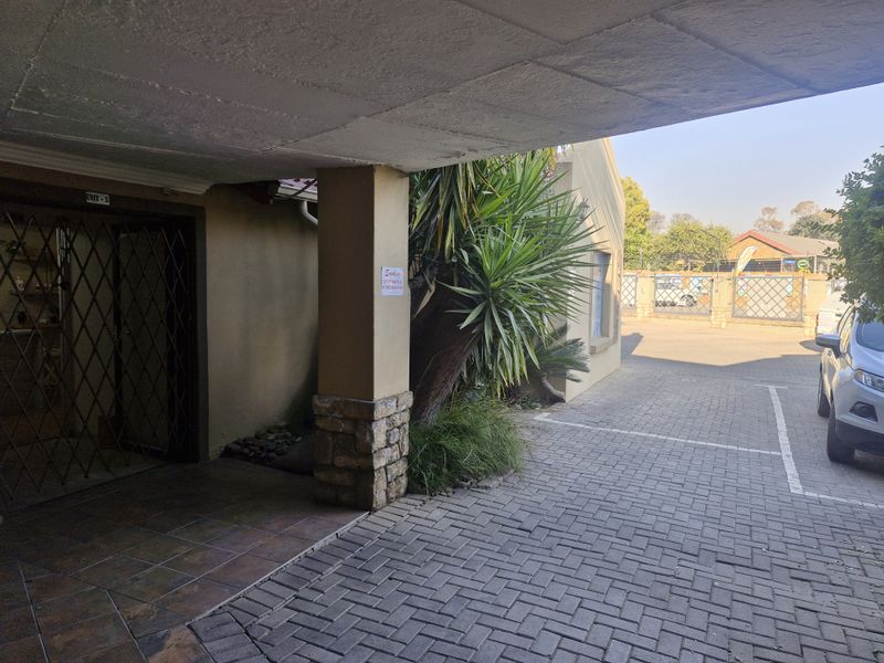 A covered entrance area featuring a paved driveway, security gate, and stone-accented pillar, providing access to the commercial unit.