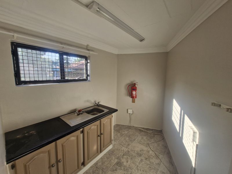 A functional utility space featuring built-in cabinetry with a stainless steel sink, tiled flooring, and a security-grille window.