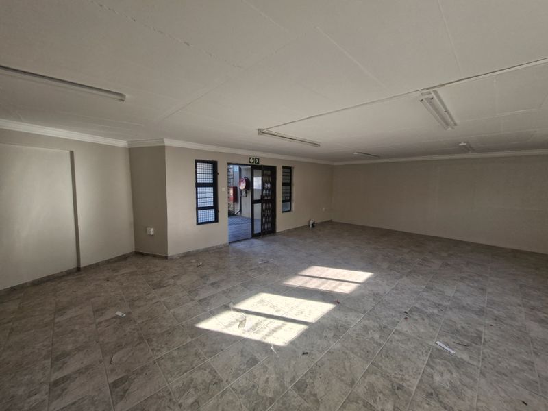 A spacious, empty open-plan commercial area featuring tiled flooring, fluorescent lighting, and a secure entrance gate.