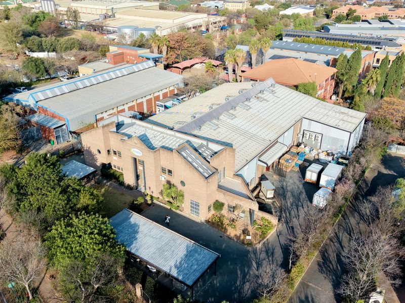 Aerial view of an industrial property featuring a large warehouse structure with metal roofing, brick facade, and paved access areas.