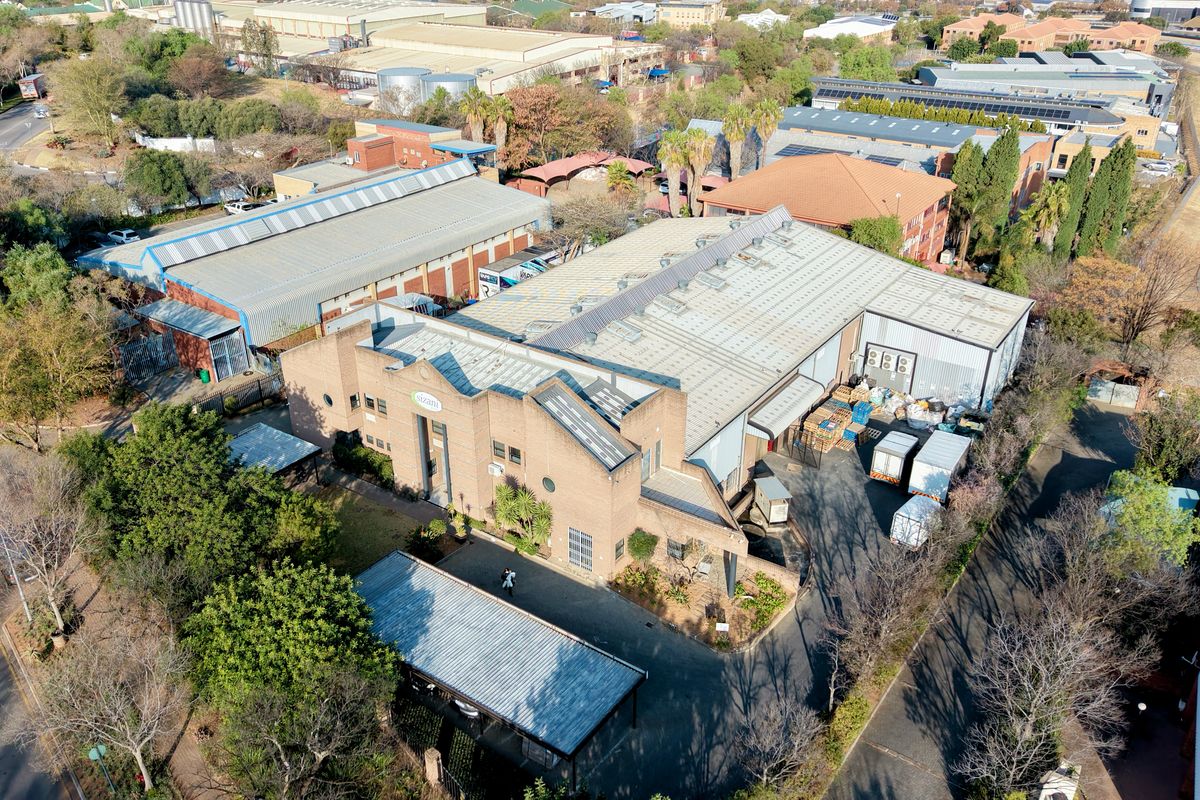 Aerial view of an industrial property featuring a large warehouse structure with metal roofing, brick facade, and paved access areas.
