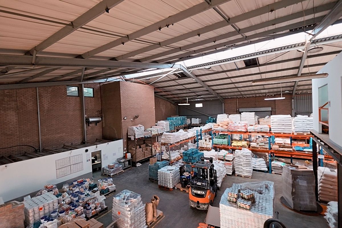 Spacious industrial warehouse featuring high ceilings with exposed steel trusses, concrete flooring, and extensive built-in racking systems for storage.