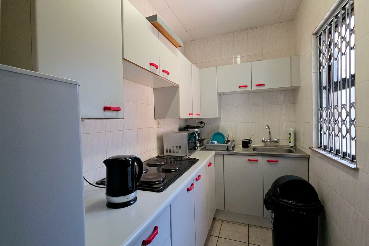 Compact kitchen featuring built-in cabinetry, an electric hob, stainless steel sink, and tiled finishes throughout.