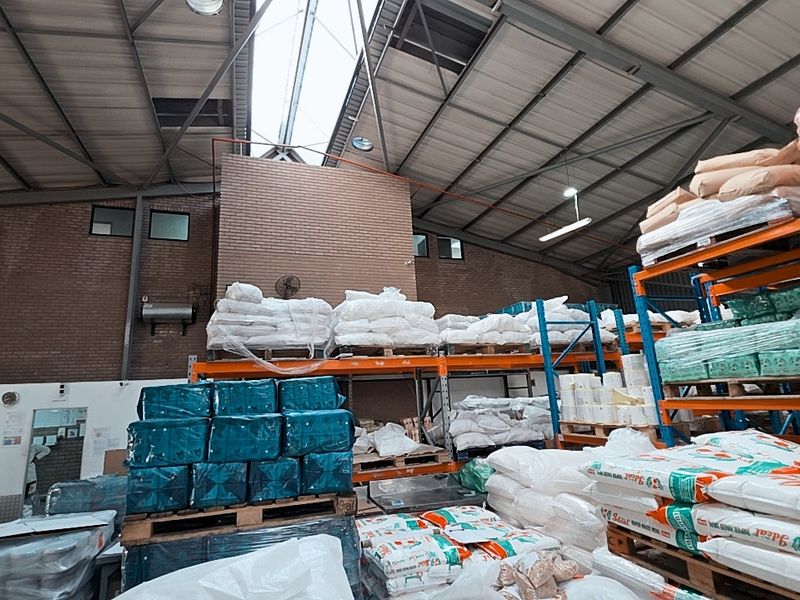Spacious industrial warehouse featuring high ceilings with exposed steel trusses, natural light from a central skylight, and extensive heavy-duty storage racking.