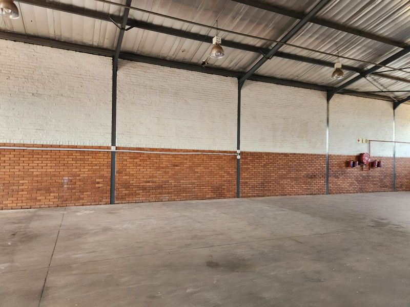 Spacious industrial warehouse unit featuring high ceilings with exposed steel trusses, durable concrete flooring, and brick wall finishes.