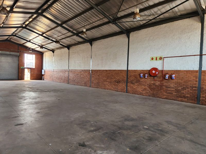 Spacious industrial warehouse unit featuring high ceilings with exposed steel trusses, concrete flooring, roller shutter access, and integrated fire safety equipment.