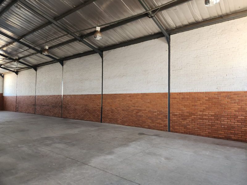Spacious industrial utility area featuring high ceilings with exposed steel trusses, concrete flooring, and a combination of painted and raw brick wall finishes.