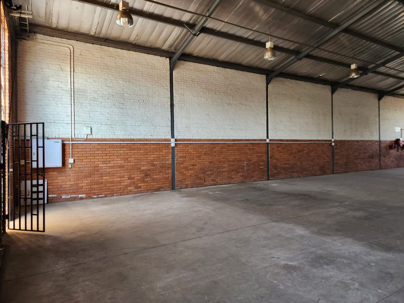 Spacious industrial utility area featuring high ceilings with exposed steel trusses, durable concrete flooring, and a combination of painted and raw brick walls.