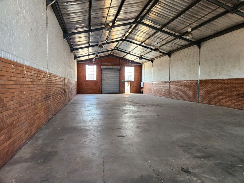 Spacious industrial warehouse unit featuring high exposed steel trusses, durable concrete flooring, and a large roller shutter door for easy access.