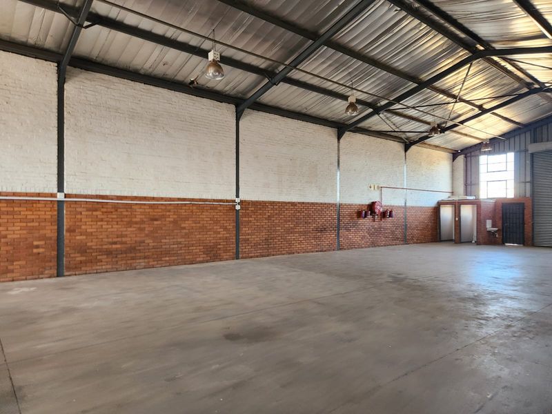 Spacious industrial warehouse unit featuring high exposed steel trusses, durable concrete flooring, brick walls, and integrated fire safety equipment.