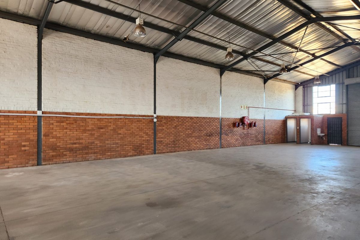 Spacious industrial warehouse unit featuring high exposed steel trusses, durable concrete flooring, brick walls, and integrated fire safety equipment.