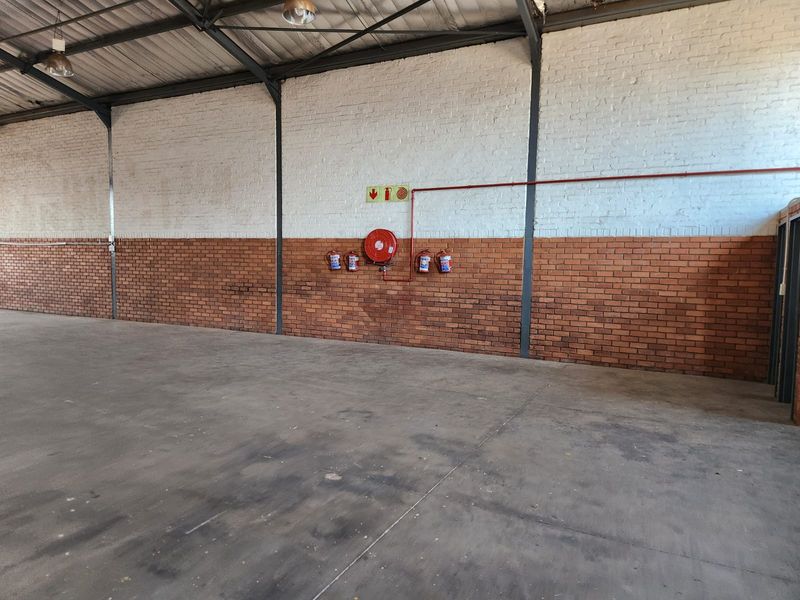 Spacious industrial warehouse unit featuring exposed steel trusses, concrete flooring, and integrated fire safety equipment including a hose reel and extinguishers.
