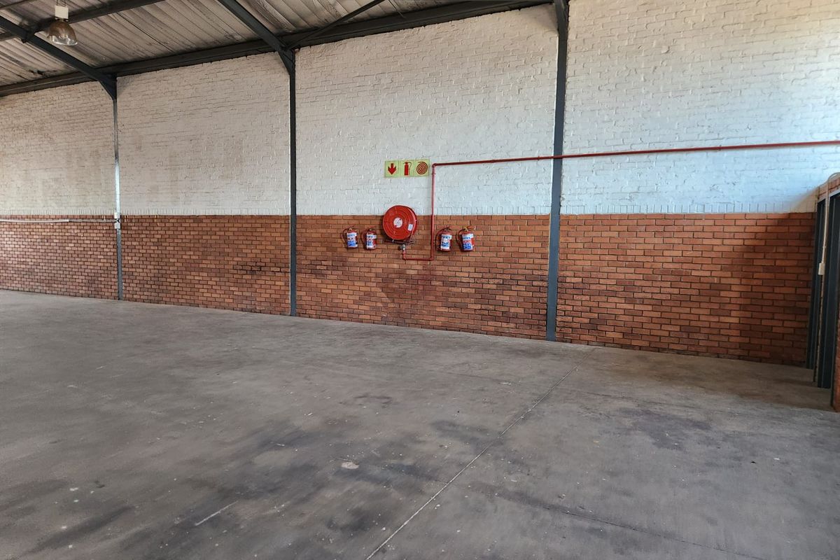 Spacious industrial warehouse unit featuring exposed steel trusses, concrete flooring, and integrated fire safety equipment including a hose reel and extinguishers.
