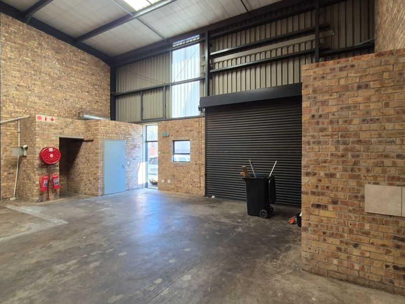 Spacious industrial utility area featuring exposed brick walls, high ceilings with steel framing, concrete flooring, and a large roller shutter door for easy access.
