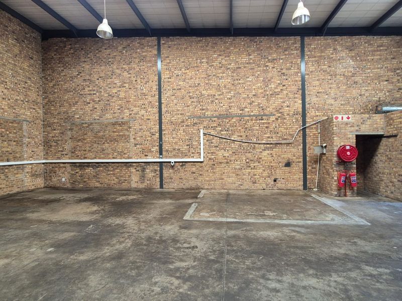 Spacious industrial utility area featuring exposed brick walls, concrete flooring, steel roof trusses, and integrated fire safety equipment.