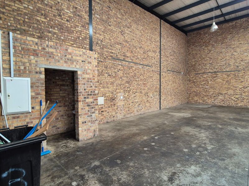 Spacious industrial utility area featuring exposed brick walls, high ceilings with steel trusses, and durable concrete flooring, suitable for storage or workshop use.