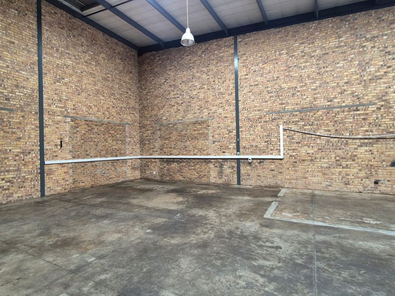 Spacious industrial utility area featuring exposed brick walls, steel structural beams, and durable concrete flooring, suitable for various commercial or storage applications.