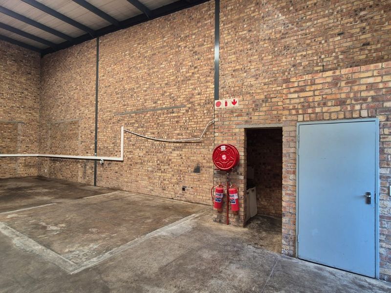 Spacious industrial utility area featuring exposed brick walls, concrete flooring, steel roof trusses, and integrated fire safety equipment.
