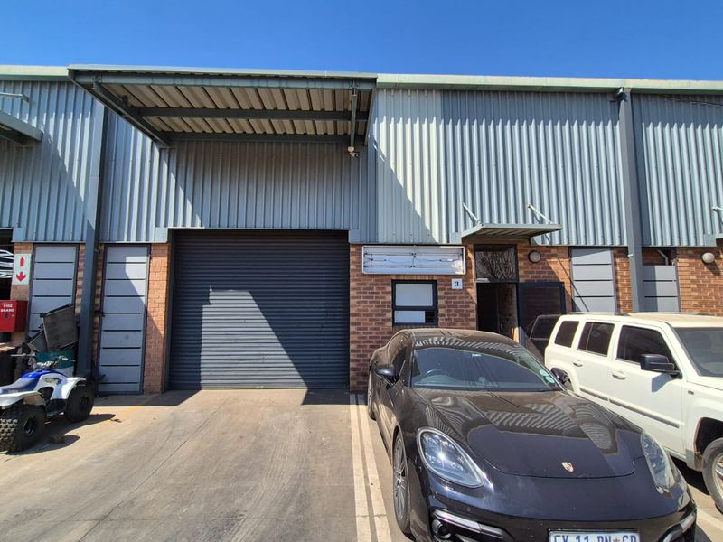 Industrial unit exterior featuring a large roller shutter door, metal cladding, and a functional entrance canopy.