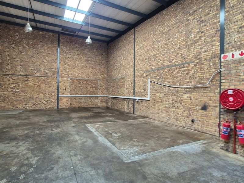 Spacious industrial warehouse unit featuring exposed brick walls, high-clearance steel portal frame, concrete flooring, and essential fire safety equipment.