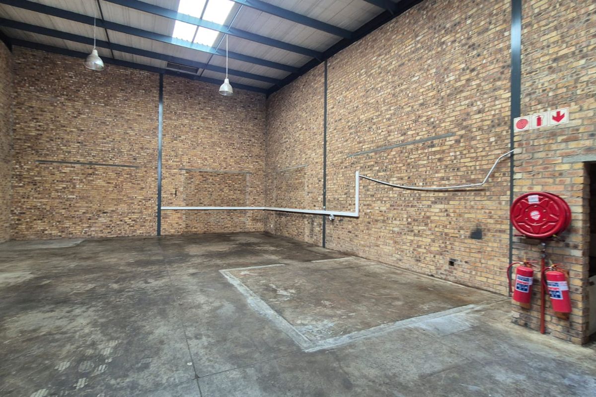 Spacious industrial warehouse unit featuring exposed brick walls, high-clearance steel portal frame, concrete flooring, and essential fire safety equipment.