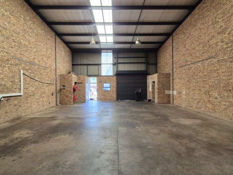 Spacious industrial warehouse unit featuring exposed brick walls, concrete flooring, high ceilings with skylights, and a large roller shutter door for easy access.