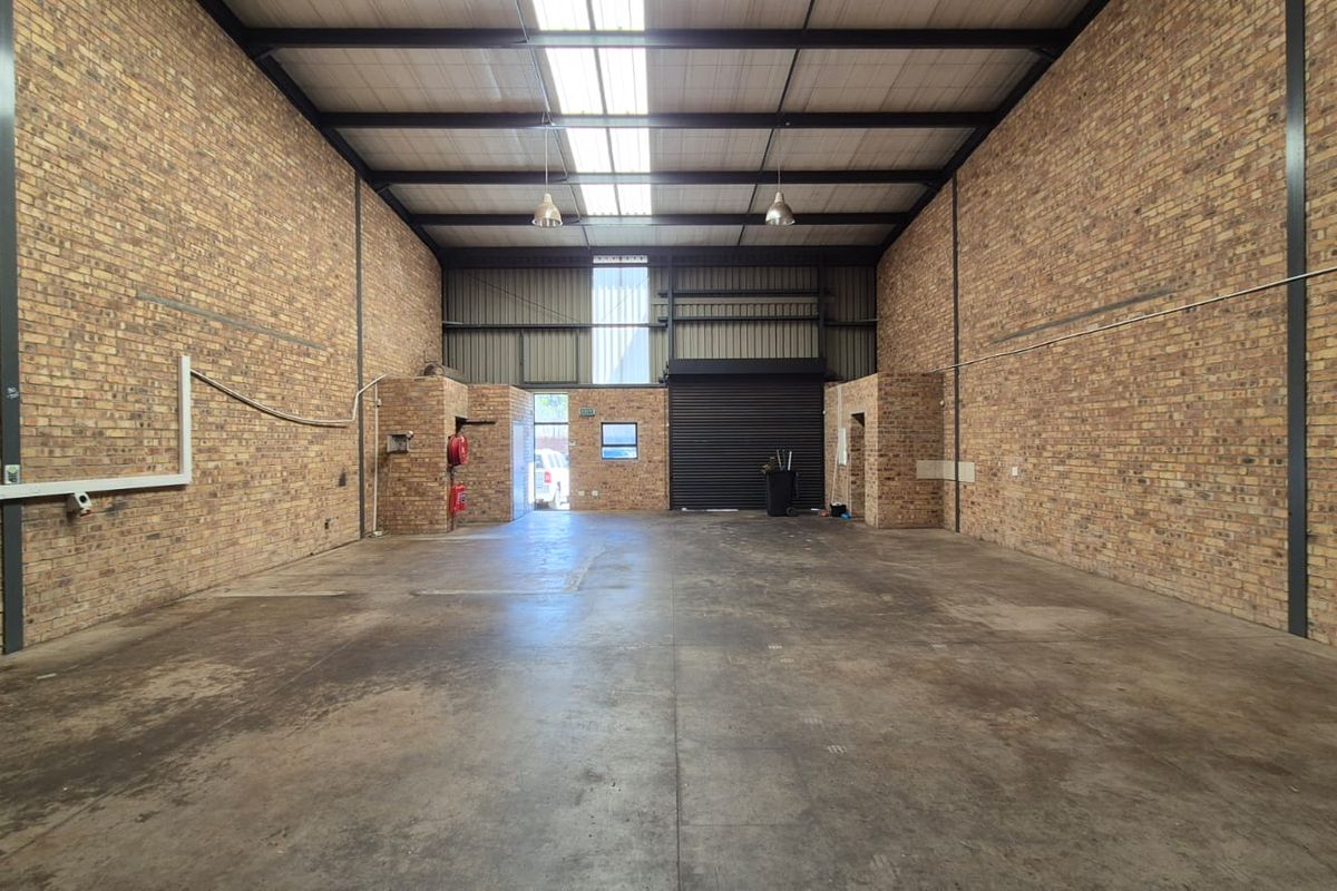 Spacious industrial warehouse unit featuring exposed brick walls, concrete flooring, high ceilings with skylights, and a large roller shutter door for easy access.