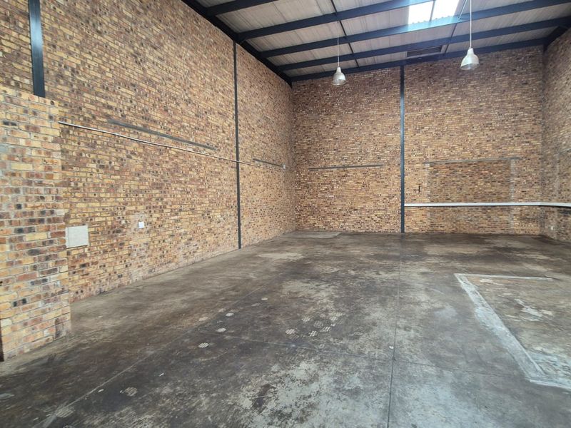 Spacious industrial utility area featuring exposed brick walls, high ceilings with steel trusses, concrete flooring, and industrial pendant lighting.