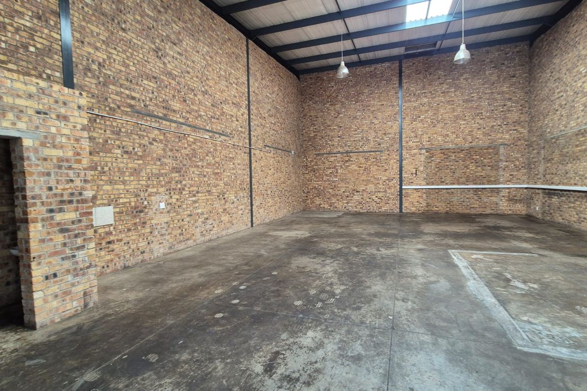 Spacious industrial utility area featuring exposed brick walls, high ceilings with steel trusses, concrete flooring, and industrial pendant lighting.