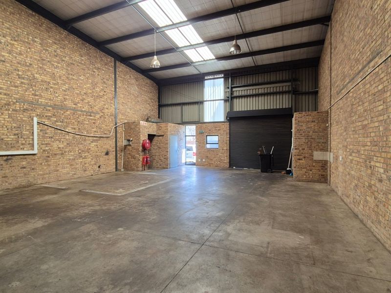 Spacious industrial warehouse unit featuring exposed brick walls, concrete flooring, high ceilings with skylights, and a large roller shutter door for easy access.