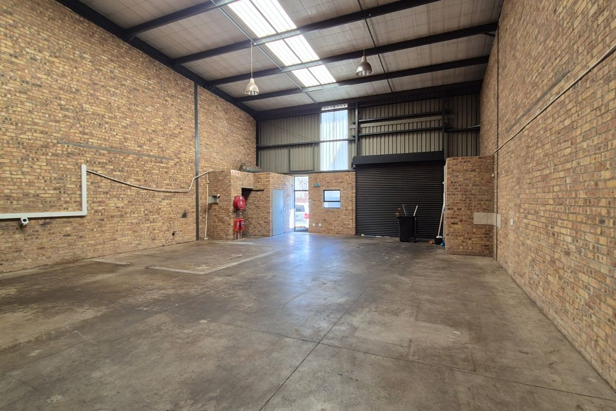Spacious industrial warehouse unit featuring exposed brick walls, concrete flooring, high ceilings with skylights, and a large roller shutter door for easy access.