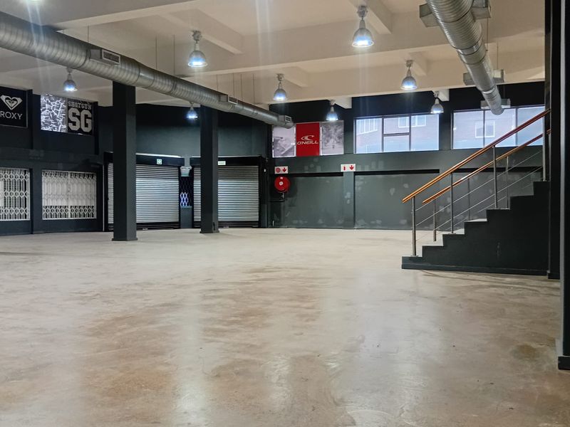 Spacious open-plan retail area featuring industrial-style exposed ducting, concrete flooring, and a staircase, suitable for a variety of commercial or retail applications.